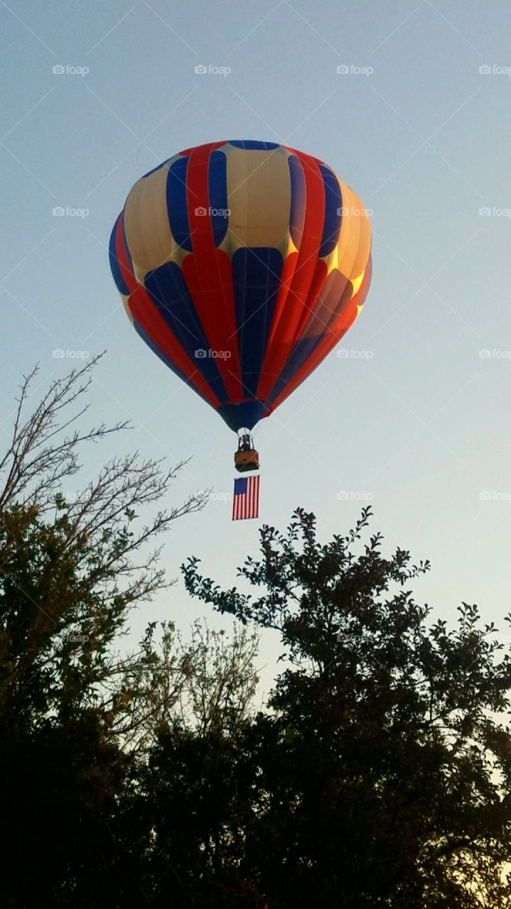 American flag hanging from a hot air balloon as it flies above the trees at dawn
