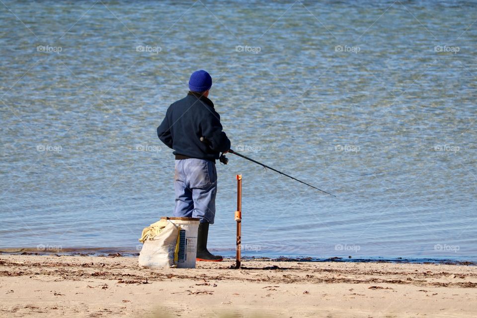 Lone fisherman in wool cap fishing off the shoreline on beach 