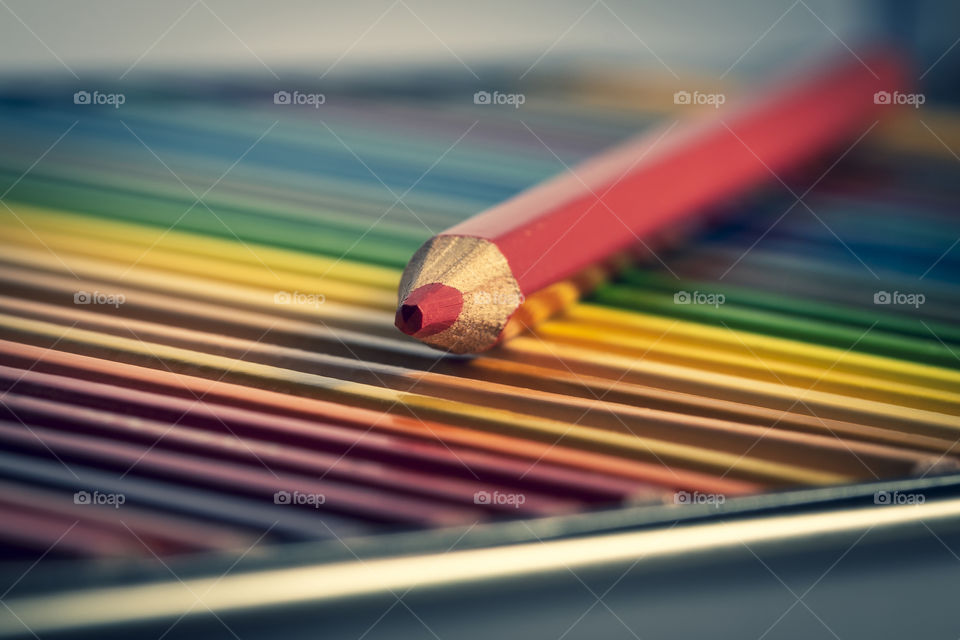 A colorful portrait of a red colored pencil lying on top of a lot of other colored pencils in a box filled with pencils to color and create with.