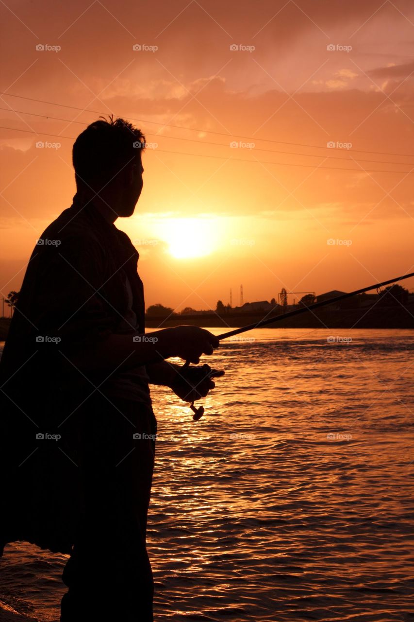 silhouette of a fisherman against the backdrop of the setting sun by the lake. photo without a face.