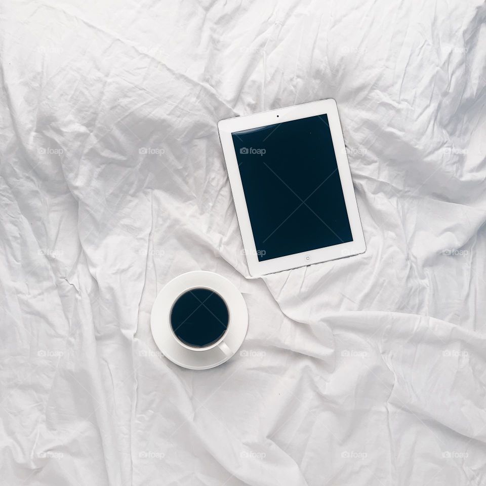 White photo. Cup of coffee with tablet on bed