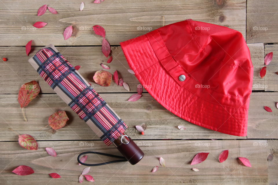 Red hat with umbrella on wooden background with fall leaves