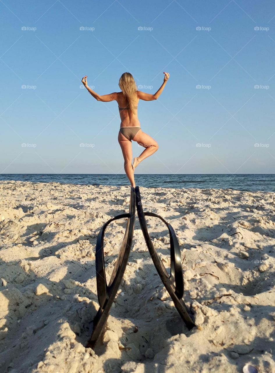 White blonde girl stands in yoga balance position at the beach 