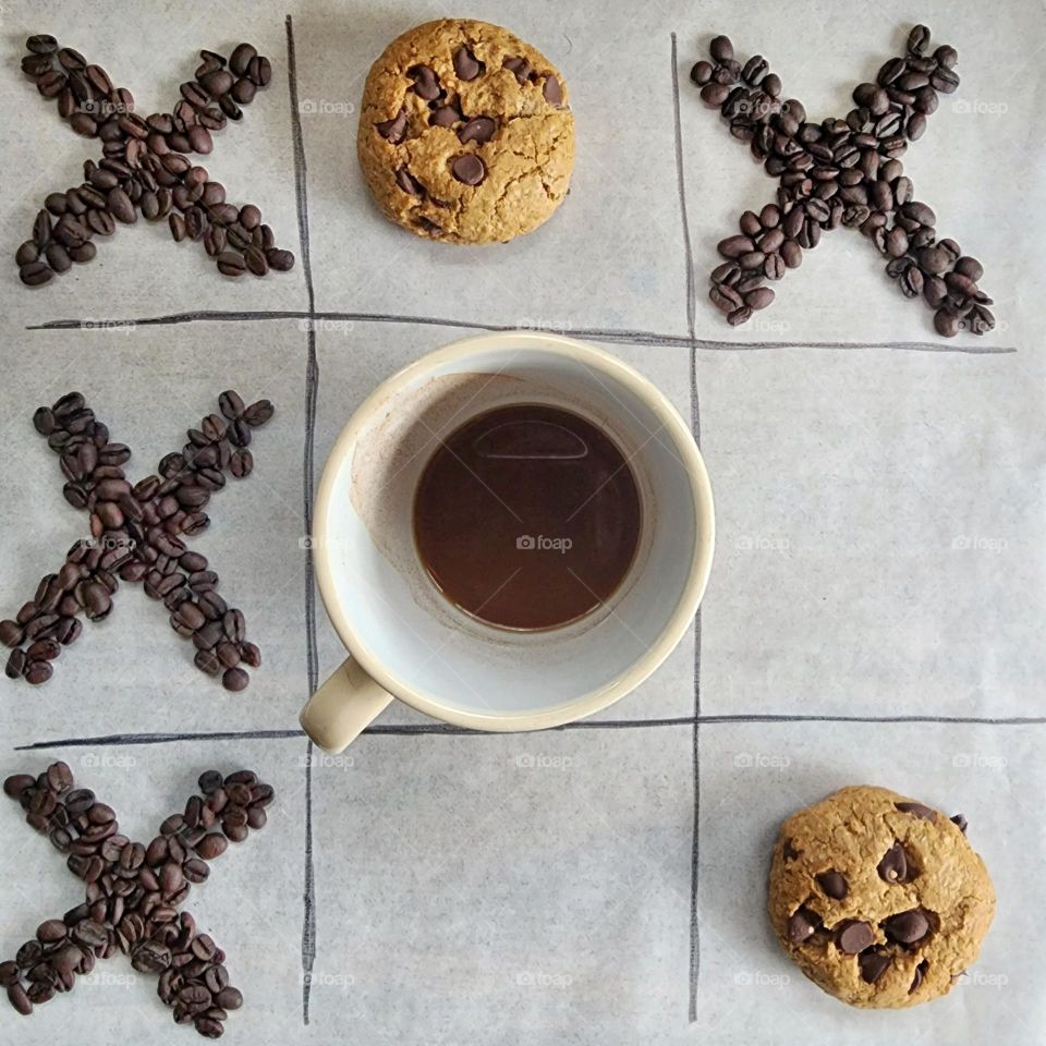 Tic Tac Toe with espresso beans, a cup of coffee, and espresso chocolate chip cookies.