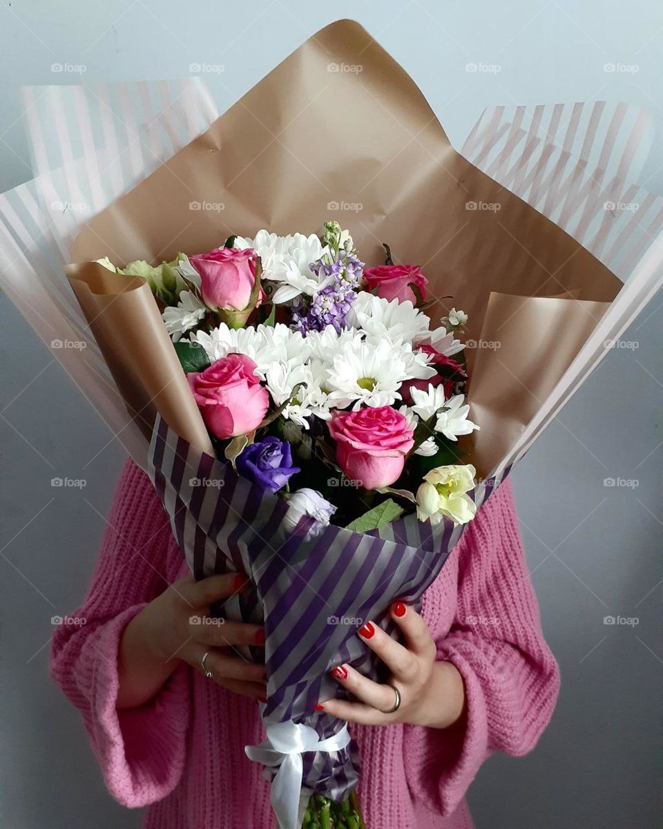 A girl in a bright pink sweater holds a large bouquet of flowers with pink roses, which creates a contrast of pink