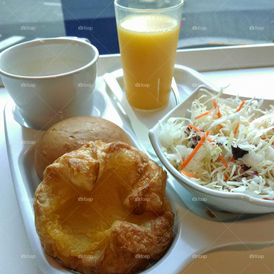 2 Bread and one bowl of salad served with orange juice on the white tray.