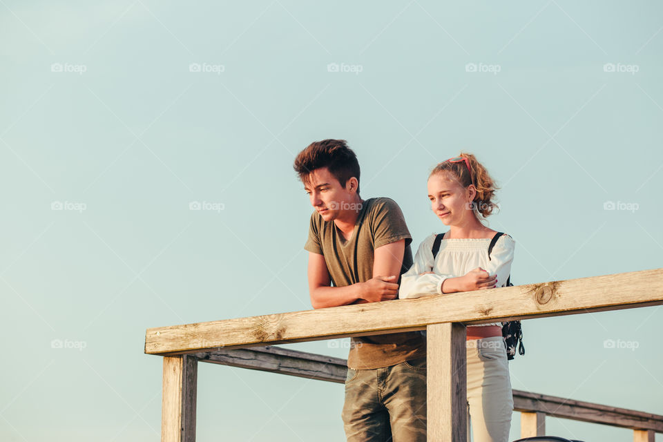 Happy smiling couple of young woman and man sitting on a pier over the sea during summer vacations. Copy space room for text