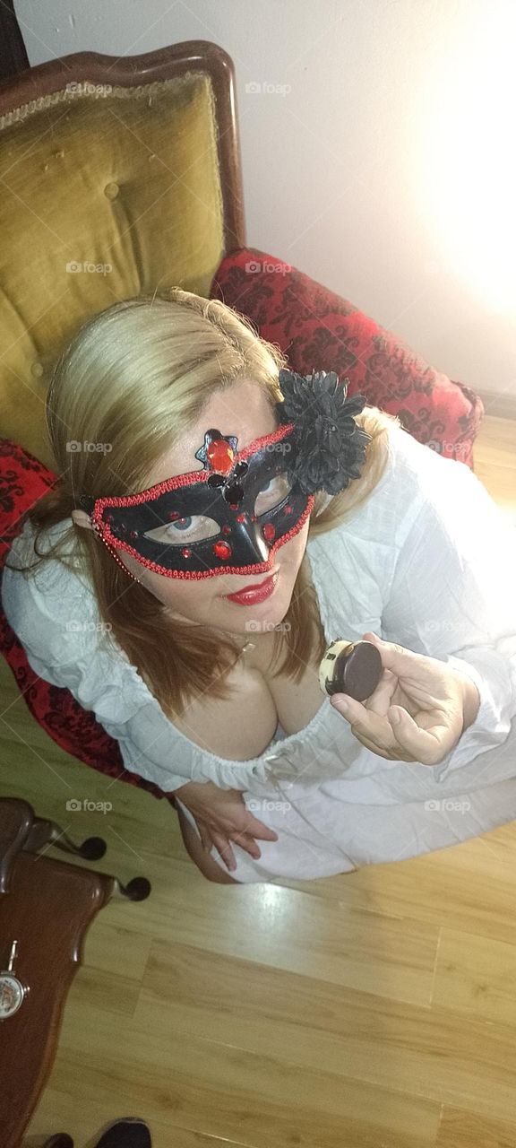 mujer con enagua y antifaz comiendo alfajor de chocolate