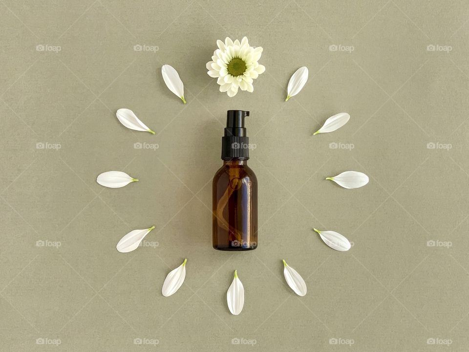 Amber glass bottle for skin cosmetic or gel sanitizer, white chrysanthemum petals, age concept