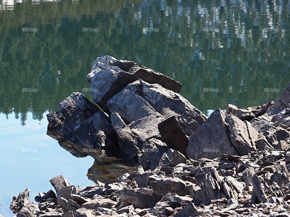 Jagged rocks and boulders along the shoreline of Ochoco Lake in Central Oregon on a sunny spring day.