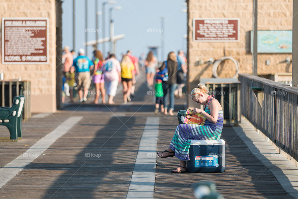 Woman reading a magazine in the sea port for fishing bridge 