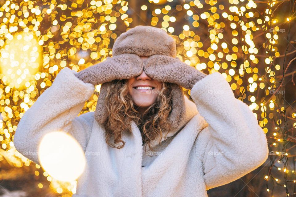 Young happy woman with curly hair in fur jacket having fun in winter street decorated with lights