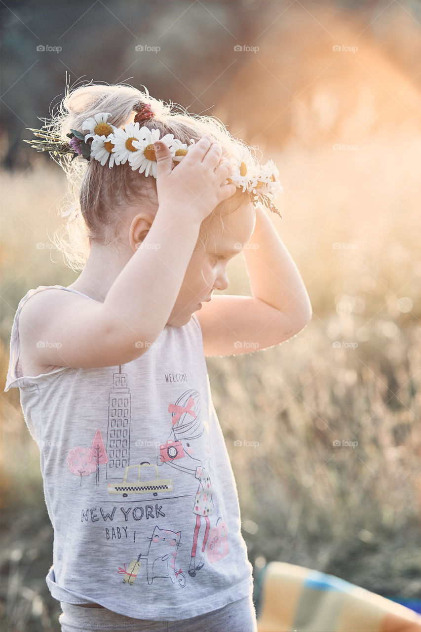 Little girl wearing a coronet of wild flowers on her head. Candid people, real moments, authentic situations