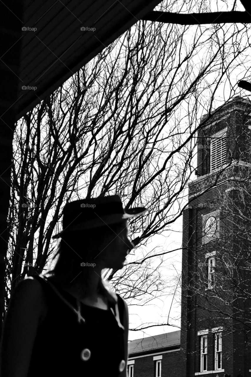 A girl or woman in the city wearing a hat and looking at the tall buildings from the shade of a tree!