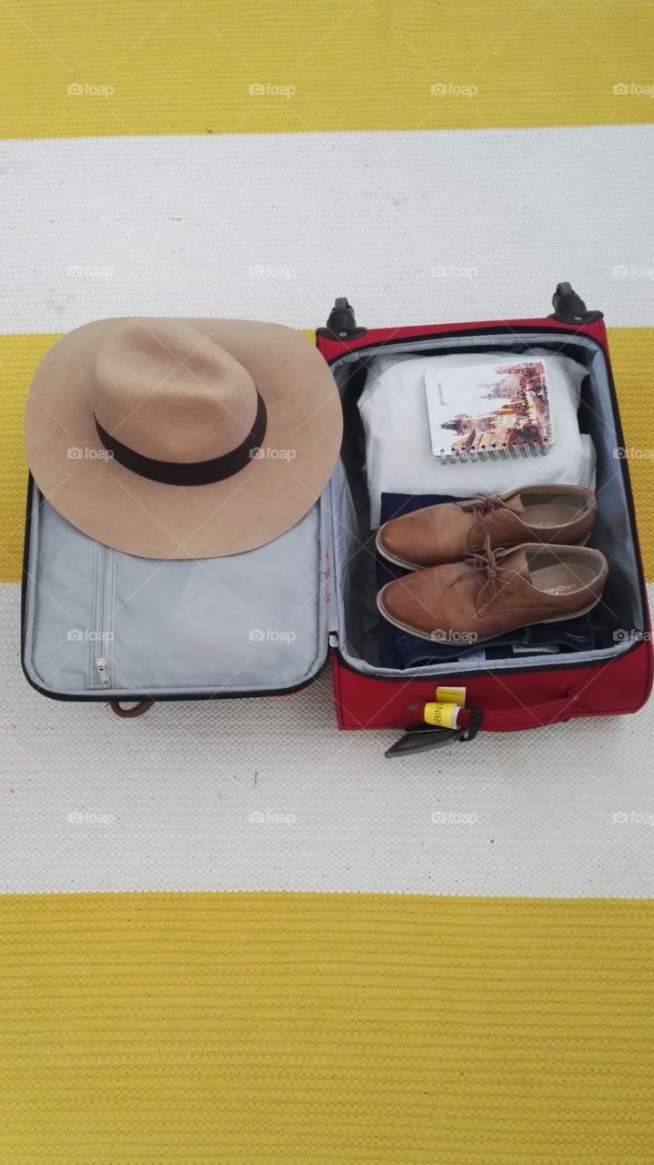 Packing simply for a vacation. Hat, brown shoes, book, white t-shirt. Red case.