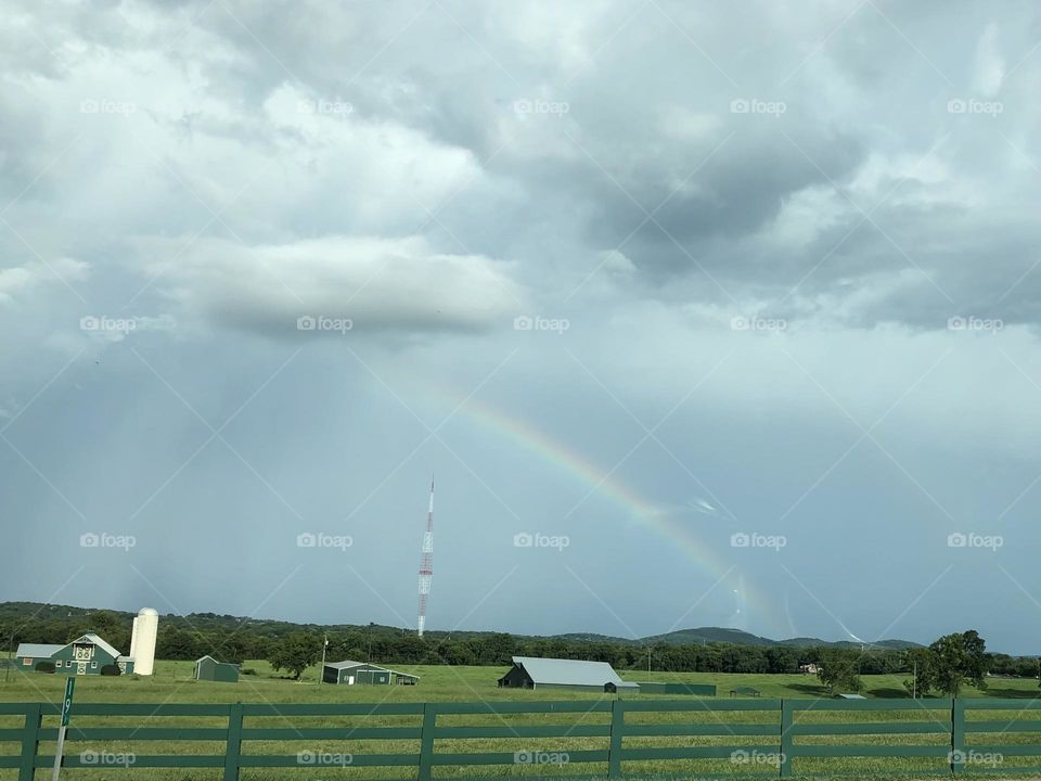 Summer cloudy sky rainbow after rain storm over farm barn green hayfields nature