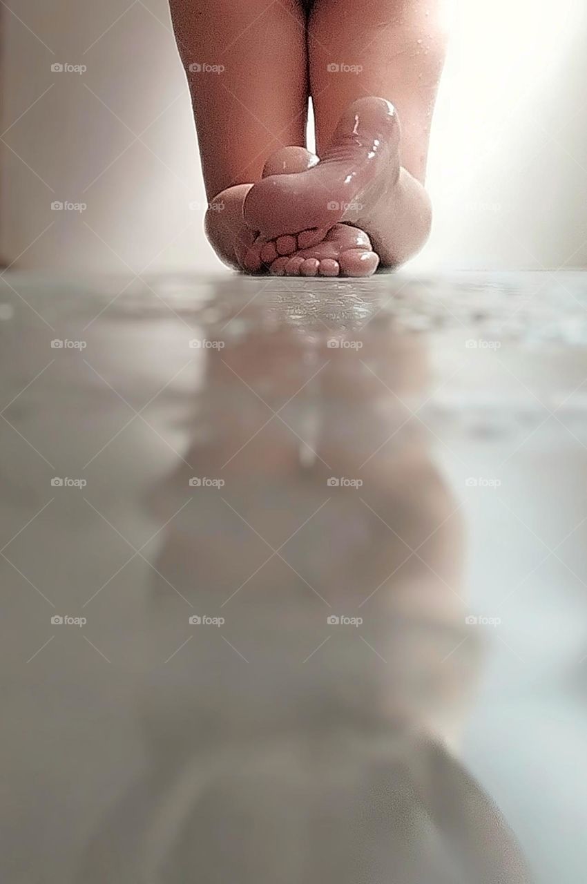 Water running down the legs and feet of a woman at bath time, exalting her curves. The shiny soles of the feet and the silhouette of the naked body projected in the shadow of the wet ground make the moment unique and very sensual.