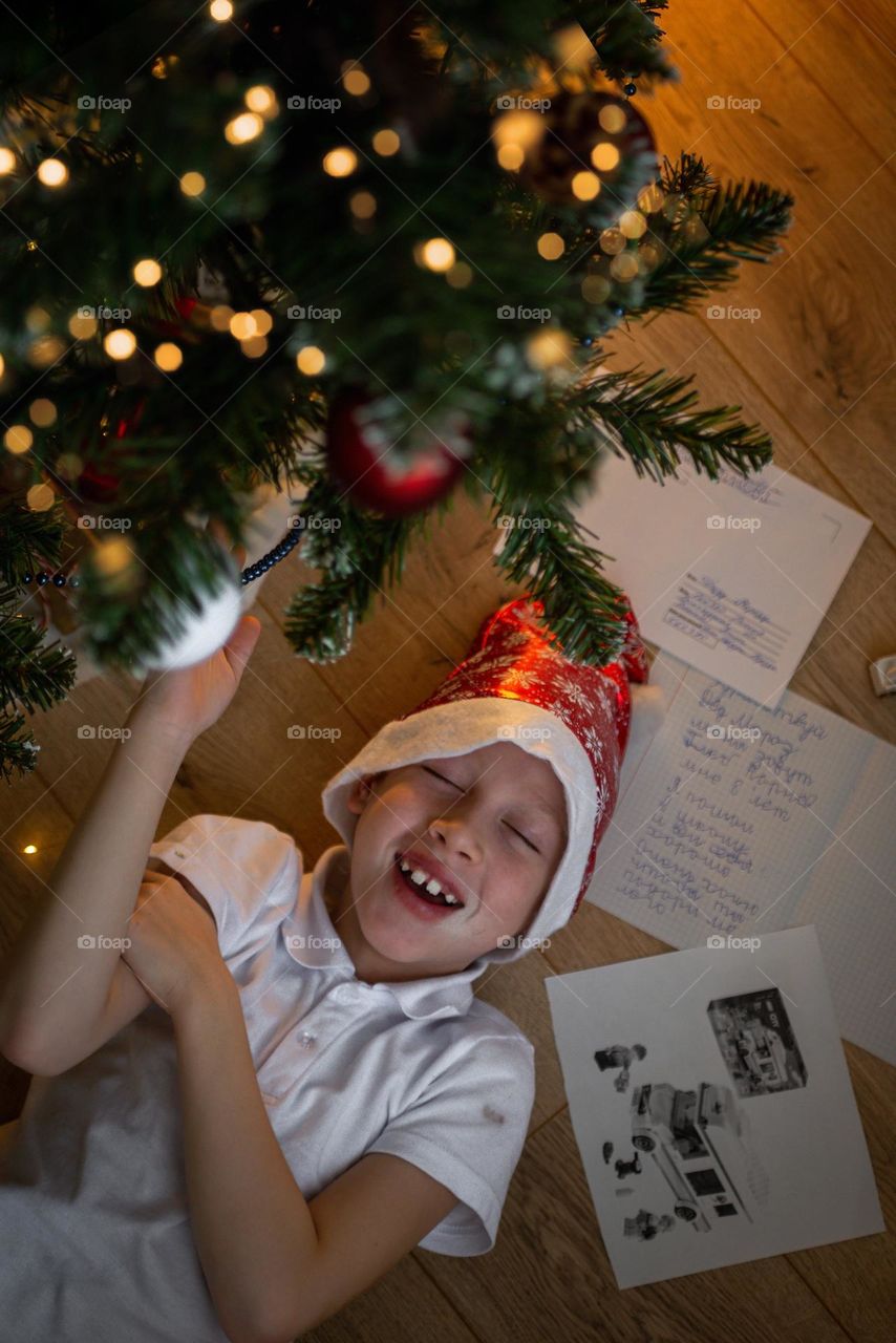 Child boy lies under the New Year tree, bright emotions surprise