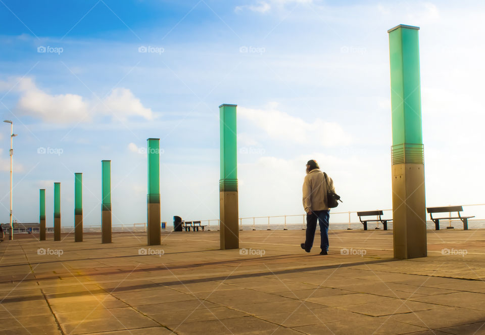 A man enjoys a stroll along the promenade at St Leonards-on-sea, past a light installation called The Stream on a bright and sunny morning
