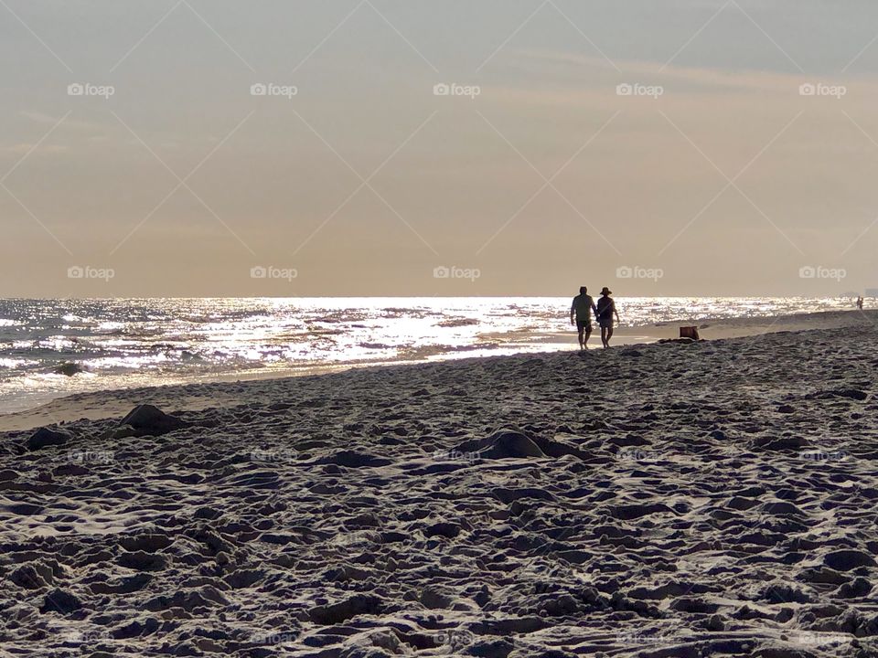 Couple in silhouette walking along seashore 