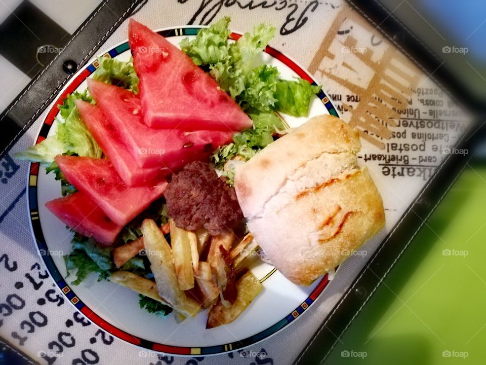 Plate with a home made burger, fries, water melon and salad