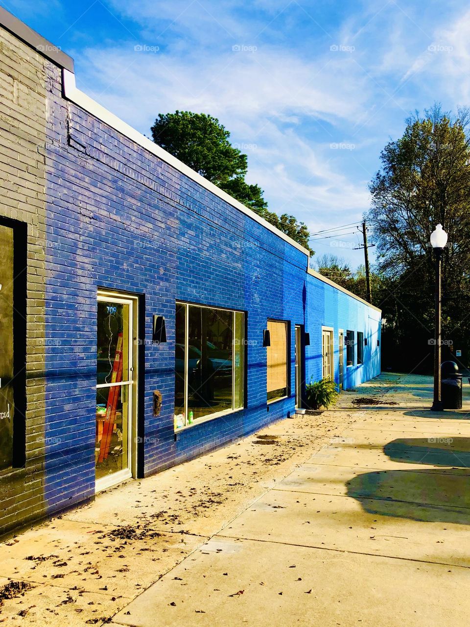 Vanishing perspective of neighborhood storefronts down a small town sidewalk. The brick is painted in successive shades of blue.