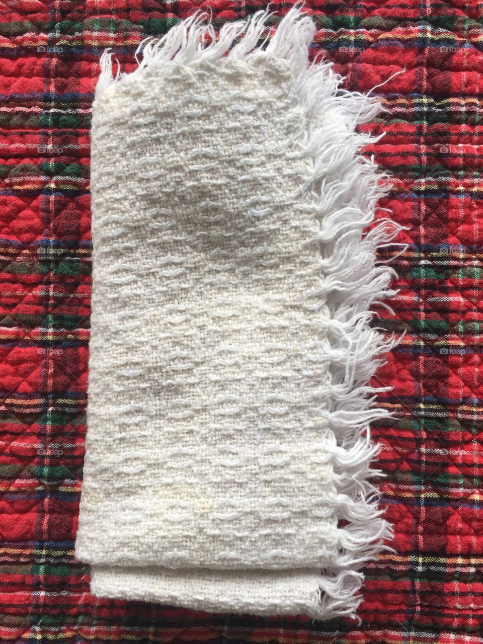 A white, fringed napkin sits on a red tartan placemat.  Both have a nice and highly visible fabric texture.