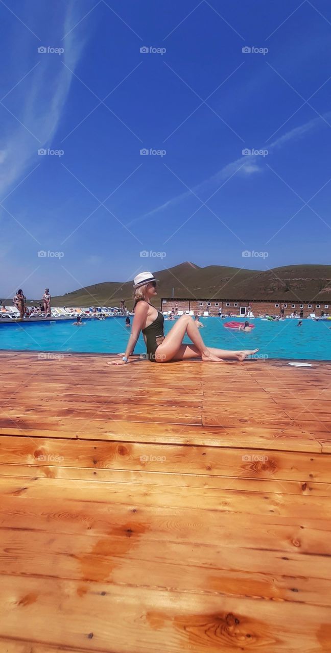 девушка в шляпе сидит около бассейна