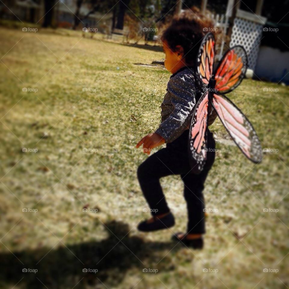 Time flutters by. A toddler pretending to be a butterfly