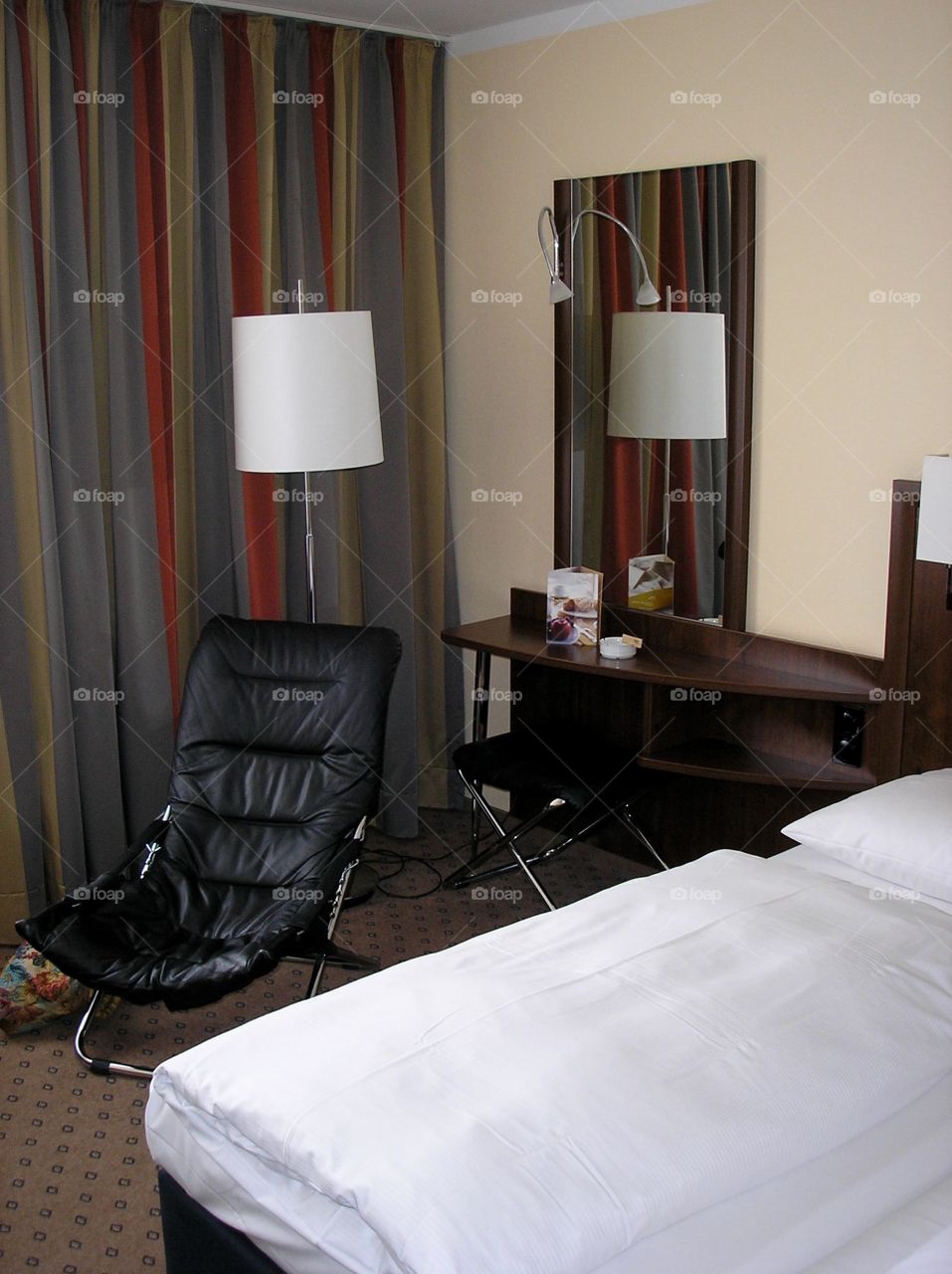 Hotel room interior with lamp, bed, chair, table, curtain and a mirror