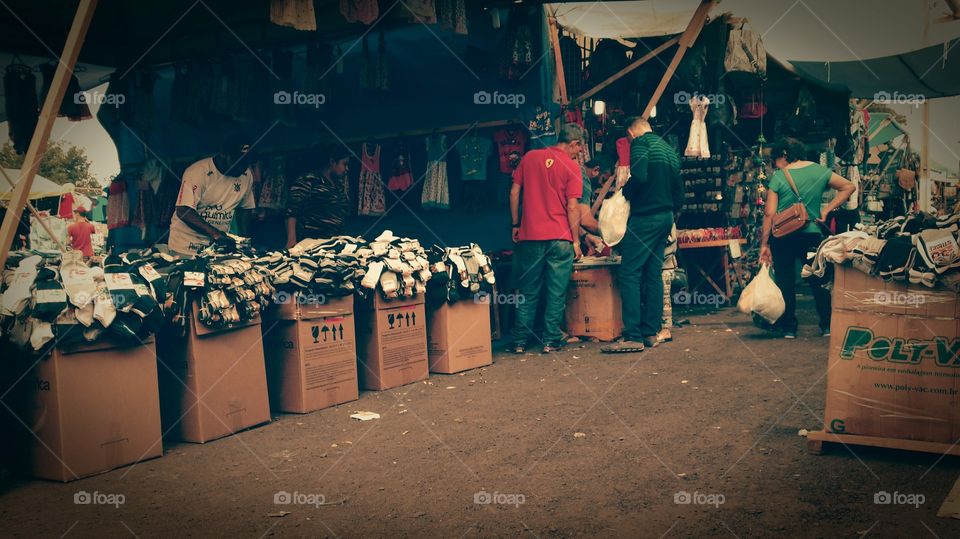 Pessoas em exposições de barracas de Camelôs, roupas e acessórios ao ar livre.