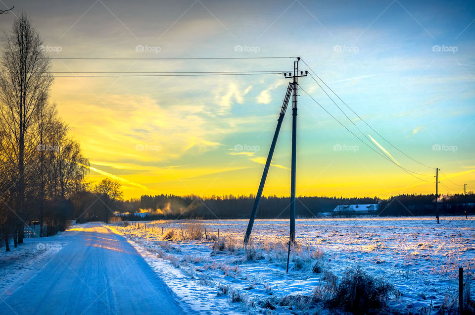 Telephone cables over a snowy country road at sunset