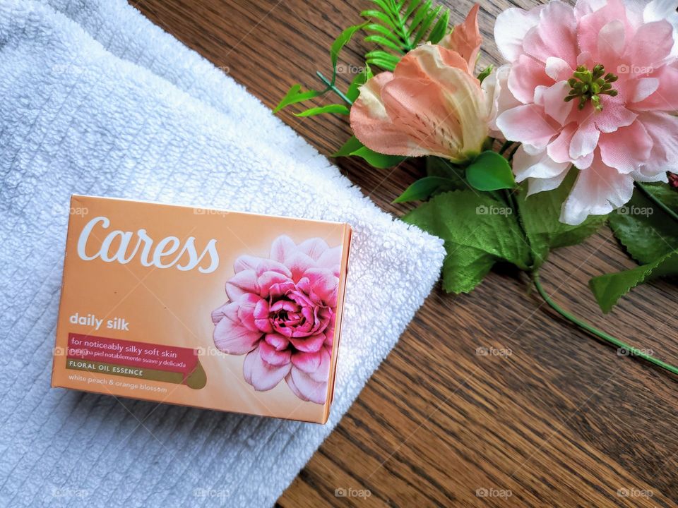 The new look Caress bar soap daily silk single bar on a white towel that is on a wood surface accented on the right top corner whith matching florals.