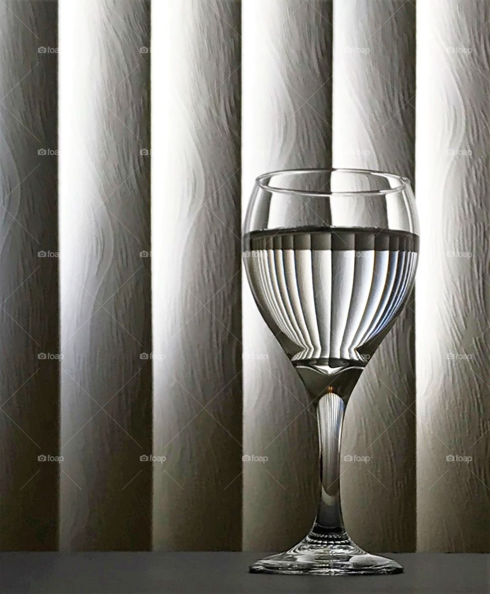 Wine glass with vertical blinds reflecting into the partially filled glass