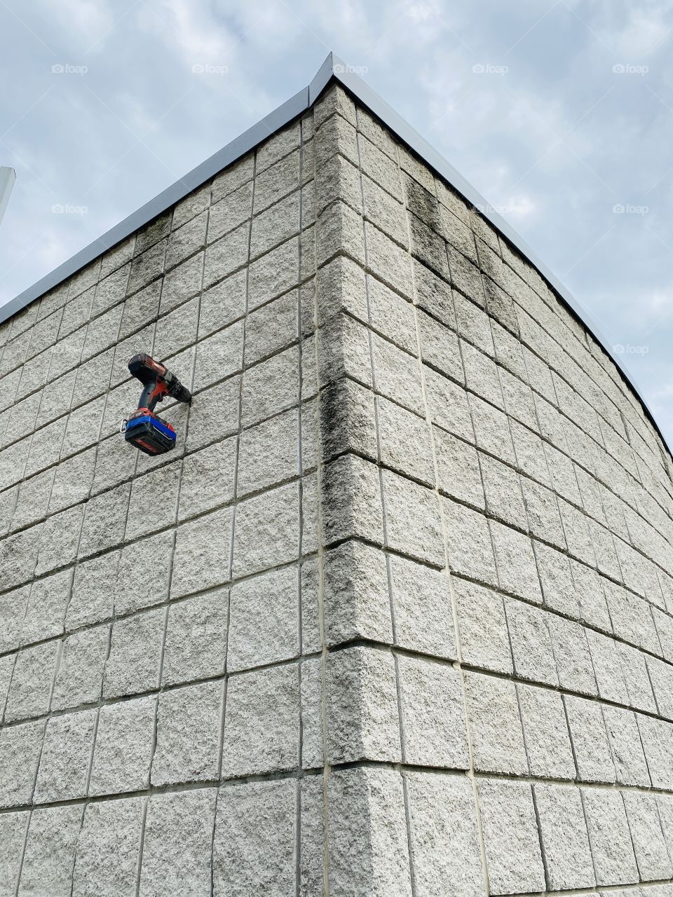 Hang in there. A drill hanging on the side of a concrete wall