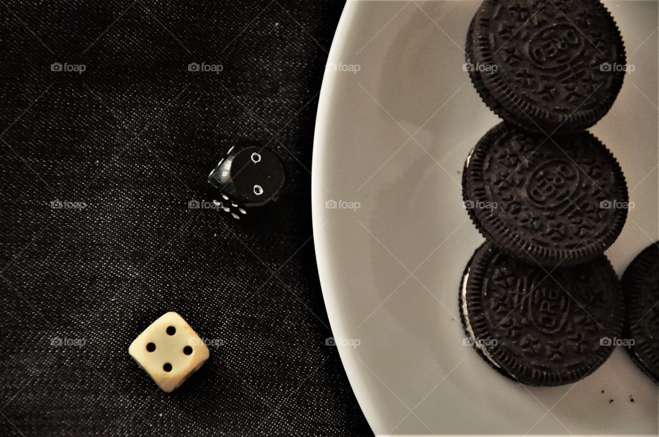 chocolate oreo cookies on white plate with black and white dices on denim surface abstract