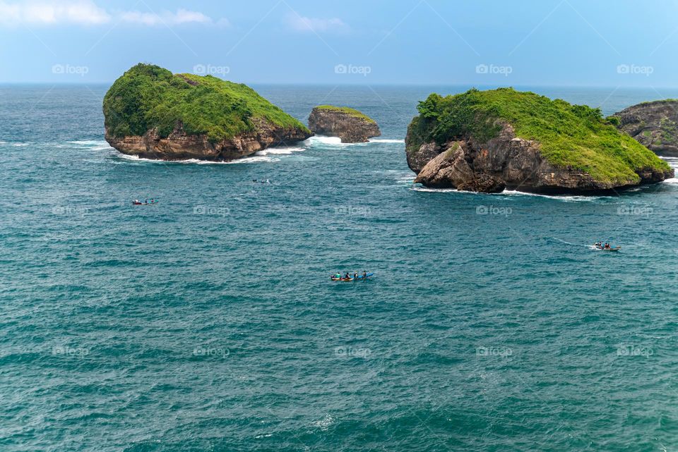 Beautiful rock formations in the middle of the sea with people on holiday using traditional boats.