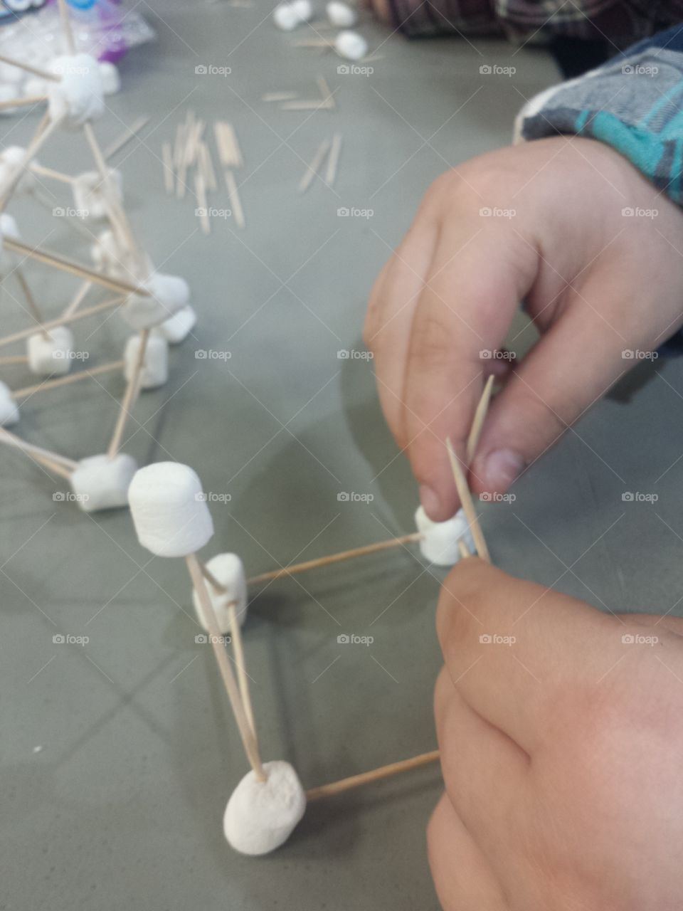 Child's hand making art with marshmallow and toothpick