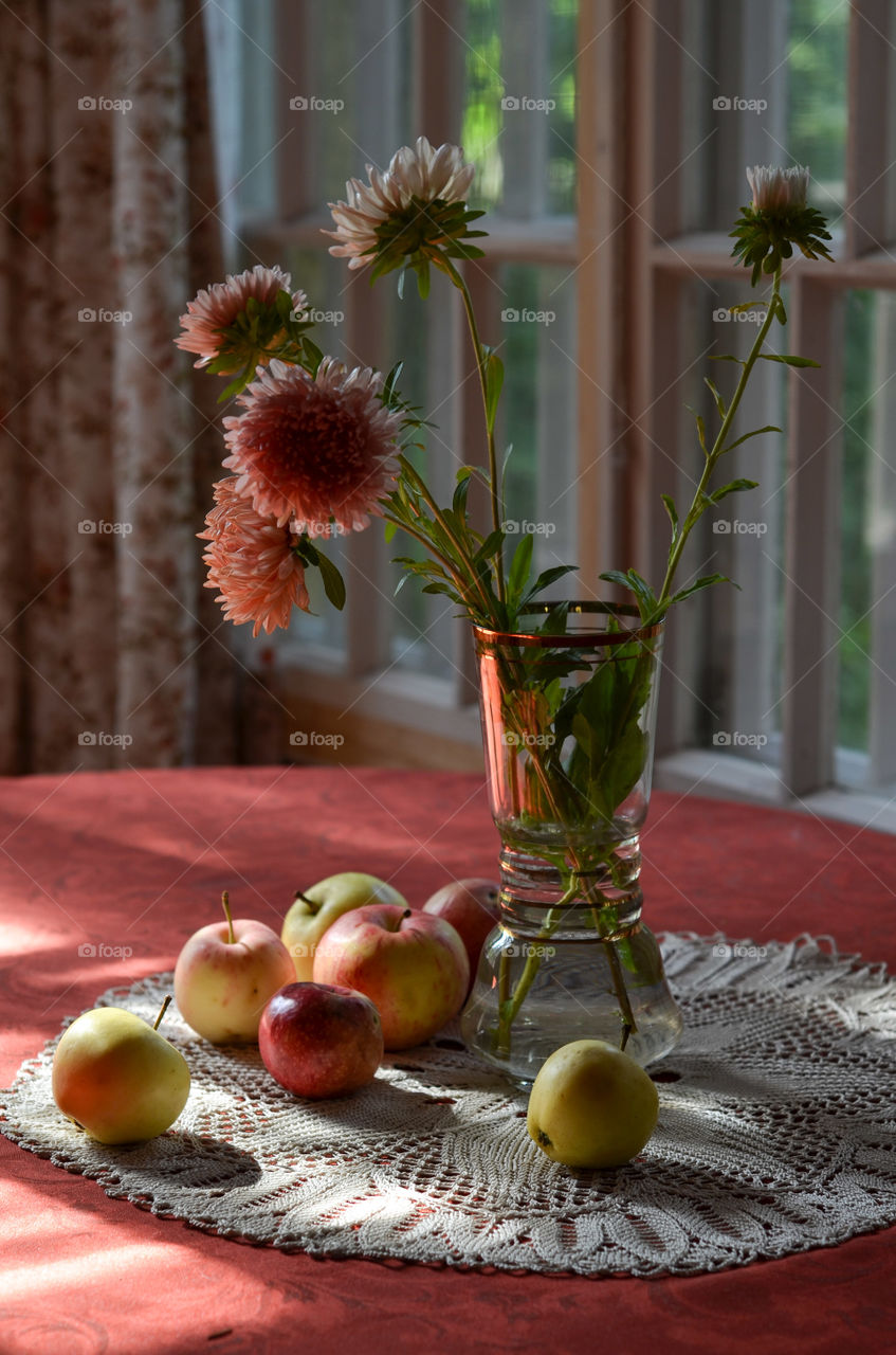 Vase with flowers and apples on the table.