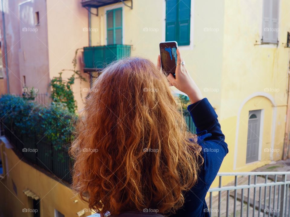 Redhead young woman taking photo with phone in the old town of Nice, France.