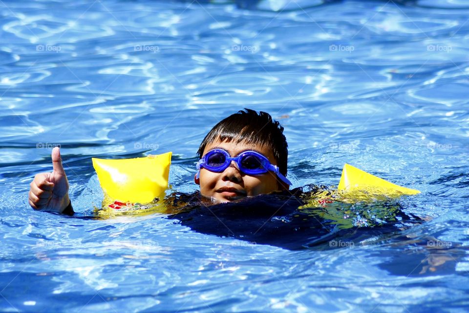 young boy in a swimming pool giving a thumbs up sign