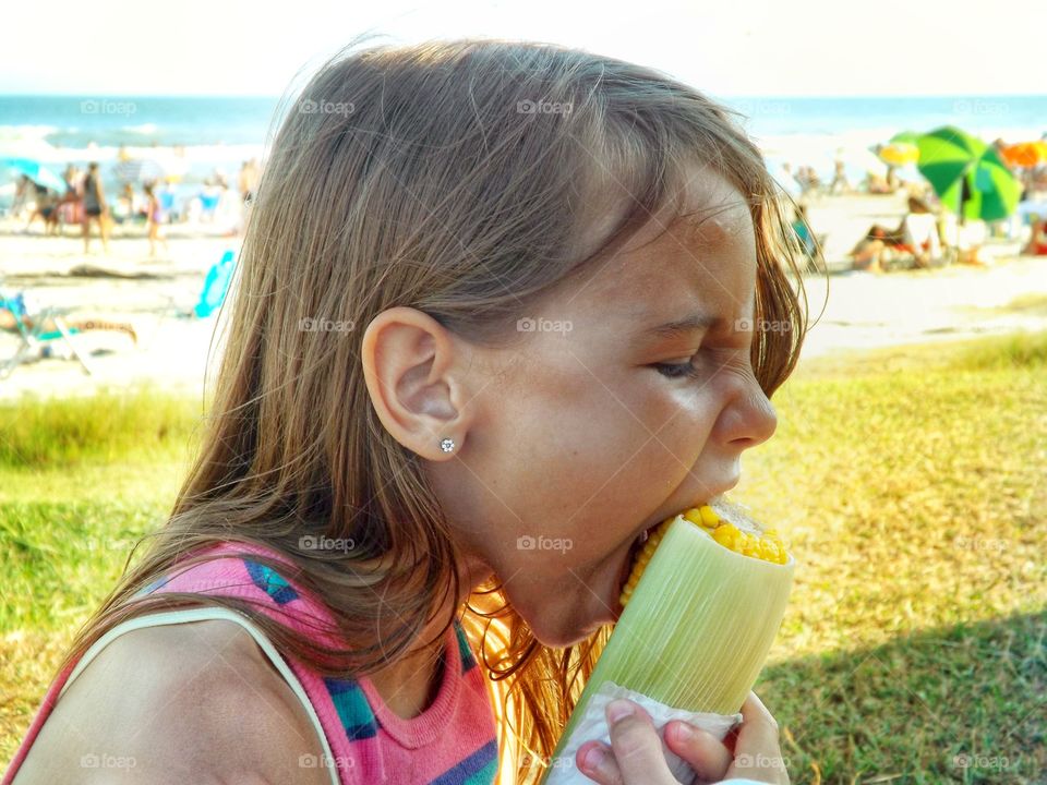 menina comendo milho na praia