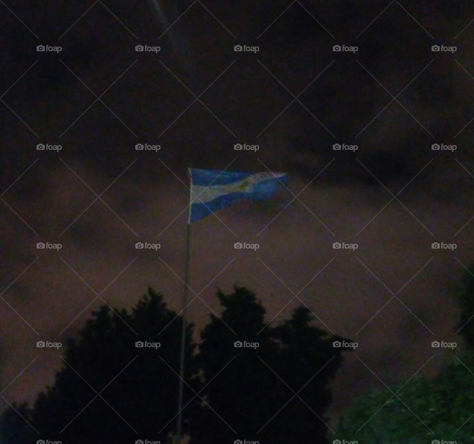 Imagen de la bandera nacional argentina, ondeando al viento en una noche tormentosa de verano