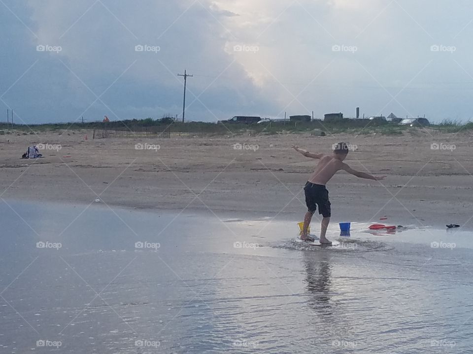 A boy skimboarding at the beach with a large Thunderhead in the background in the United States of America May 2018 hear Sea Rim Park in Texas