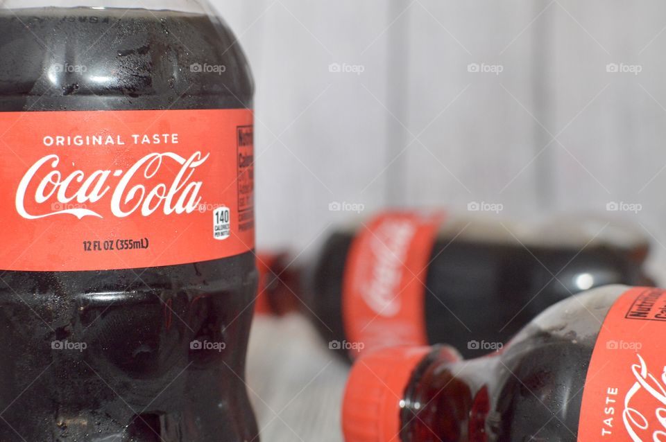 Three plastic bottles of Coca-Cola on a white rustic background