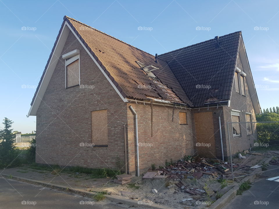 Empty, detached house. Windows boarded up with wood.