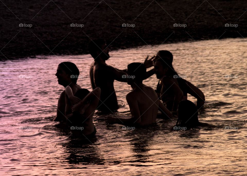 Young people having fun in the river around sunset