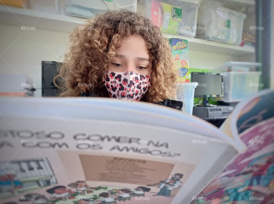 Girl in mask reading a book in the classroom.