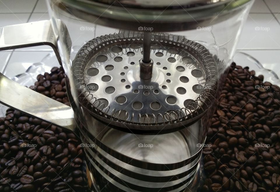 Looking inside a glass french press coffee maker at the strainer plunger sitting on whole coffee beans