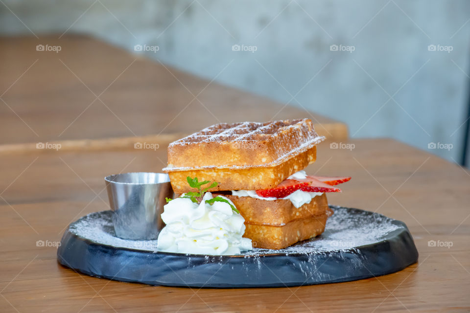 Waffle Strawerry fresh cream in the black plate on wooden table.